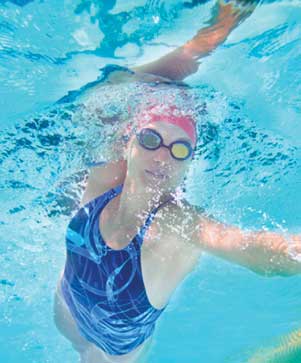 Swimmer in a red cap and goggles gliding through the water at Swimfinity Senior Learn to Delta Pool lesson